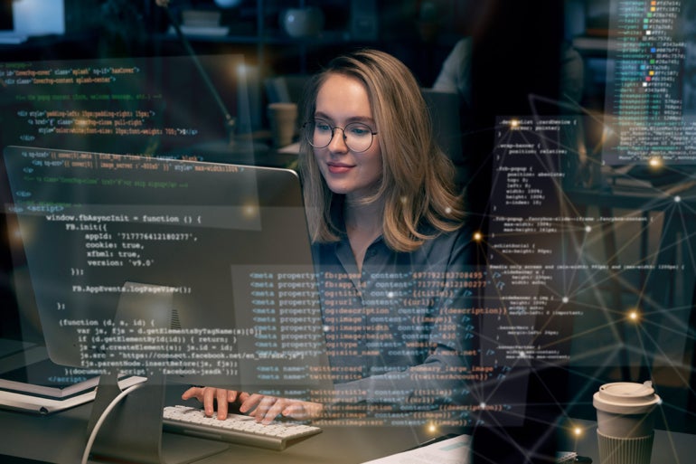 Woman programming on her desk with code blocks on virtual screen.